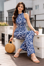 Woman in a blue floral dress sitting on a rooftop with a woven handbag.